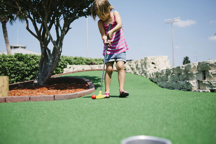 Girl playing miniature golf during sunny day