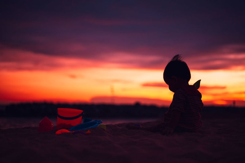 Silhouette boy on beach against sky during sunset