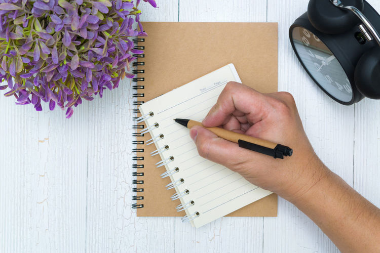 Cropped hand of man writing in book on table