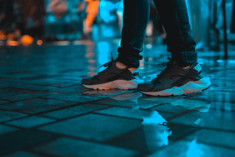 Low section of person standing on wet footpath at night