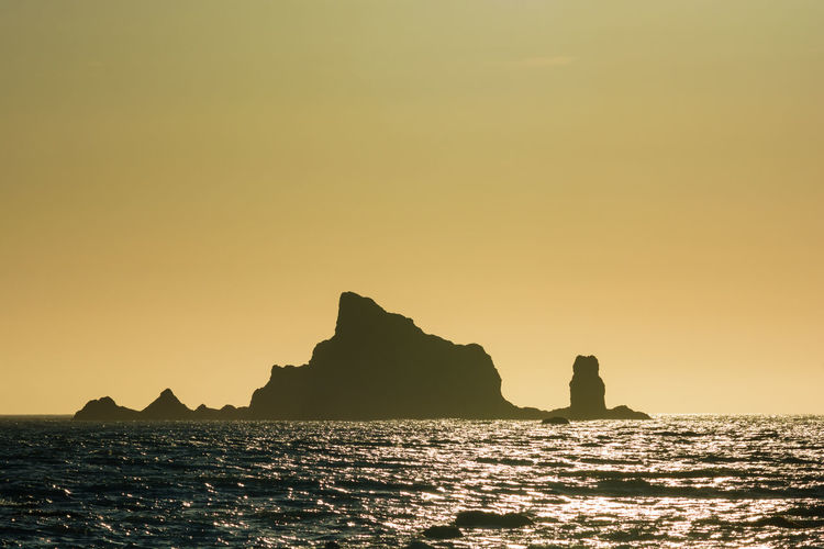 Silhouette rock formation in sea against clear sky during sunset