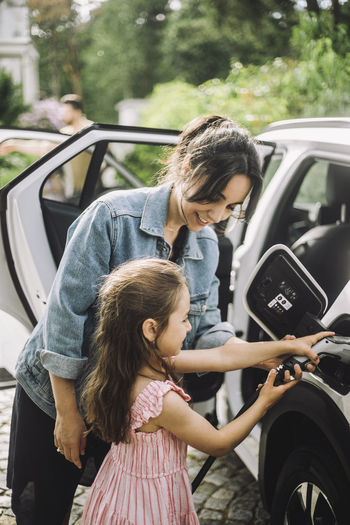 Smiling mother assisting daughter to charge electric car