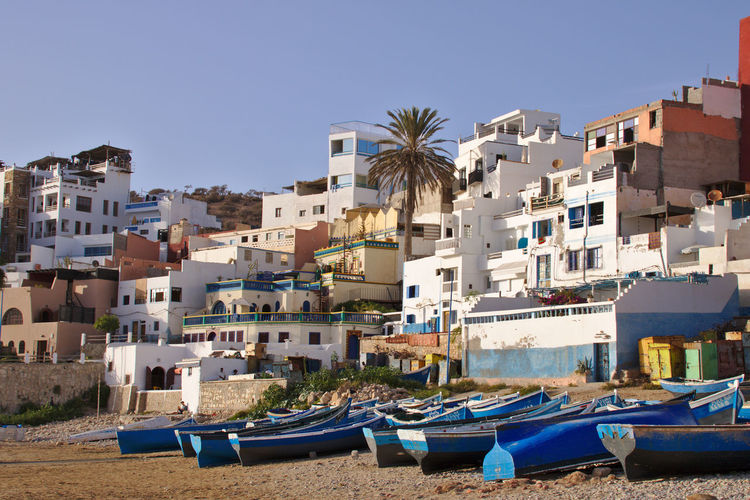 Boats moored by buildings against blue sky