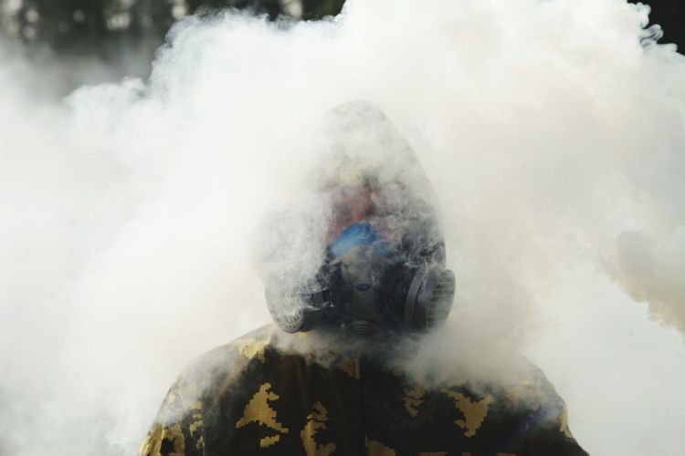 Portrait of young man in gas mask standing amidst smoke