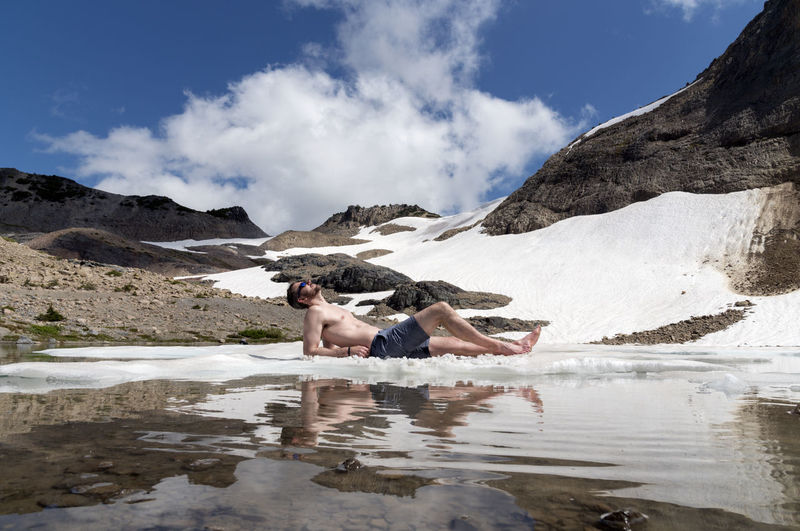 Man lying in lake against mountains during winter