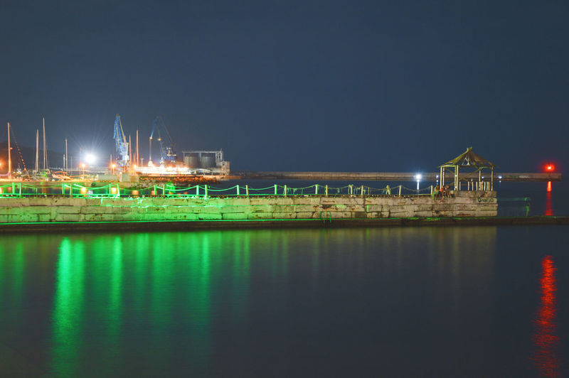 Illuminated pier over sea against clear sky at night