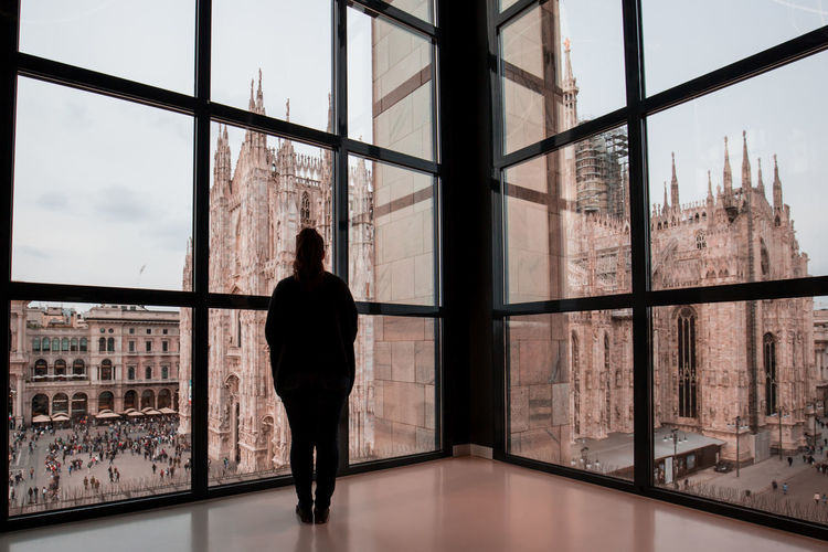 Woman looking at milan cathedral through glass window