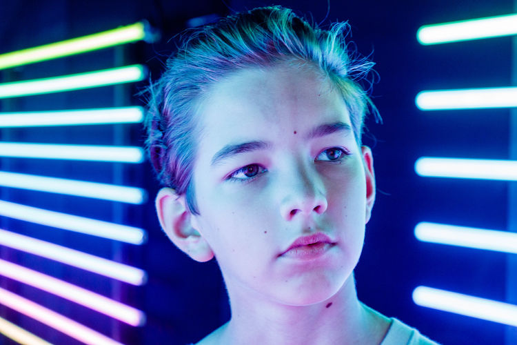 Portrait of a boy looking ahead over the background of neon lights