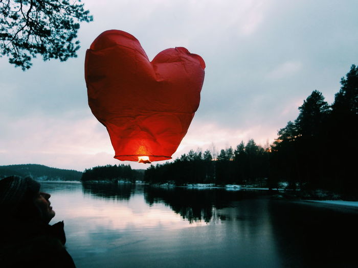 Illuminated heart shape paper lantern over lake against cloudy sky