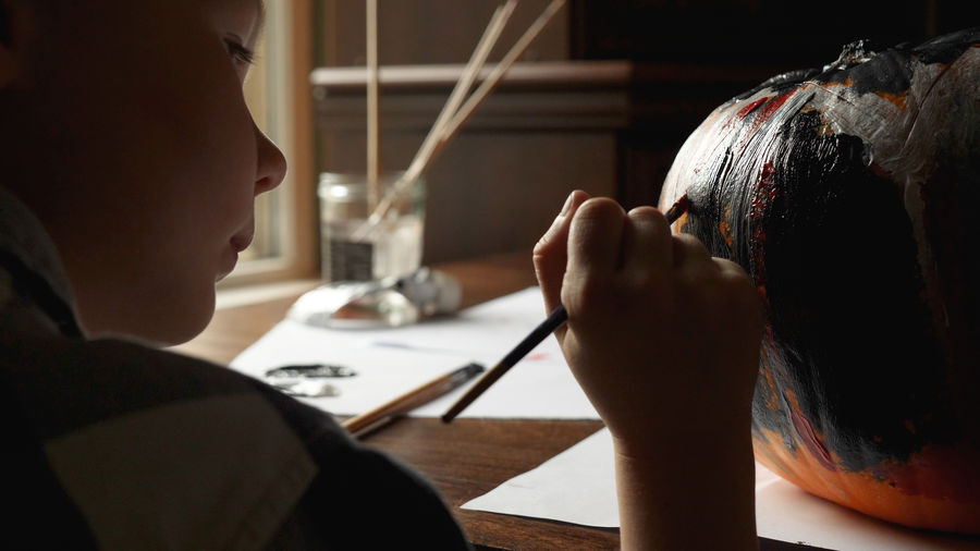 Close-up of boy painting jack o lantern at home