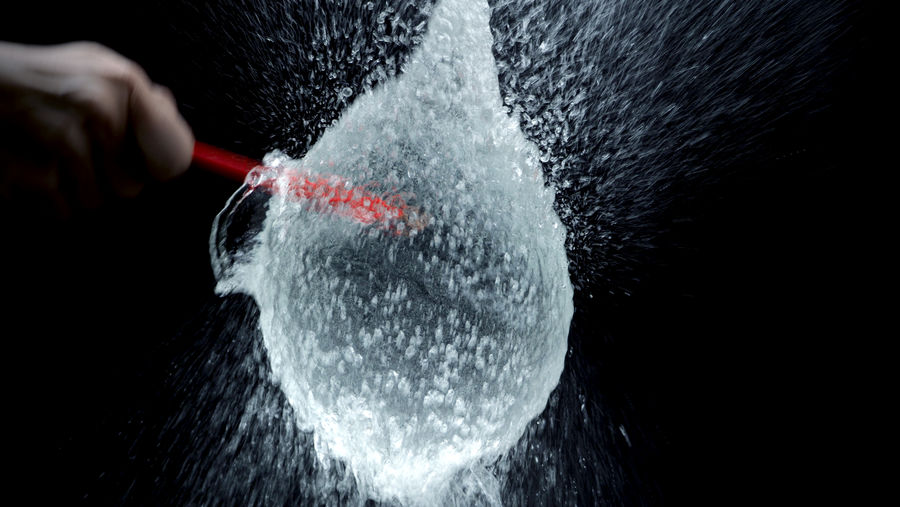 Cropped hand of person exploding water bomb against black background