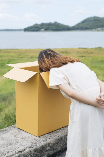 Rear view of young woman looking into cardboard box against lake