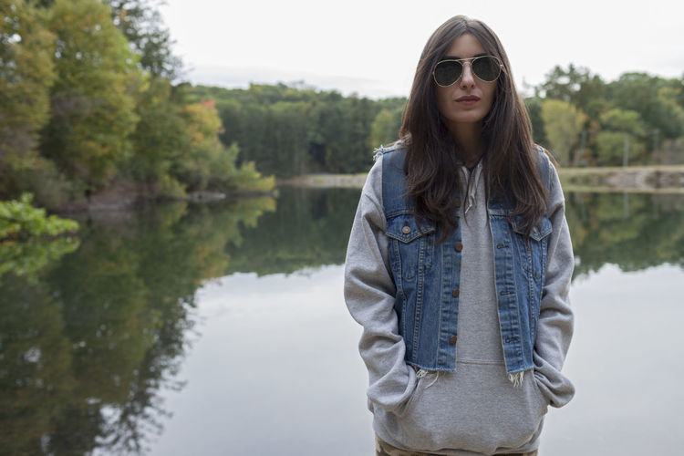 Portrait of young woman wearing sunglasses standing by lake