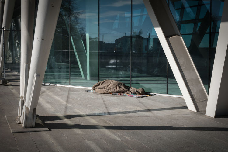 Homeless sleeping under warm blankets over a modern design bridge.