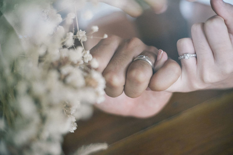 Close-up of couple taking pinky promise by flowers at home