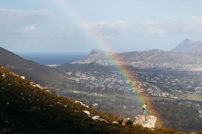Man standing on mountain by rainbow against landscape