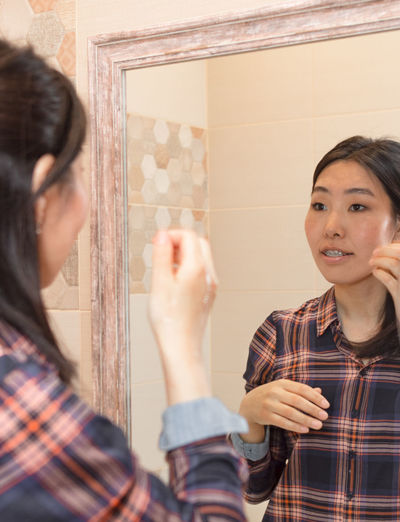 Woman with braces looks in bathroom mirror at home, casual hygiene and daily cleansing concept