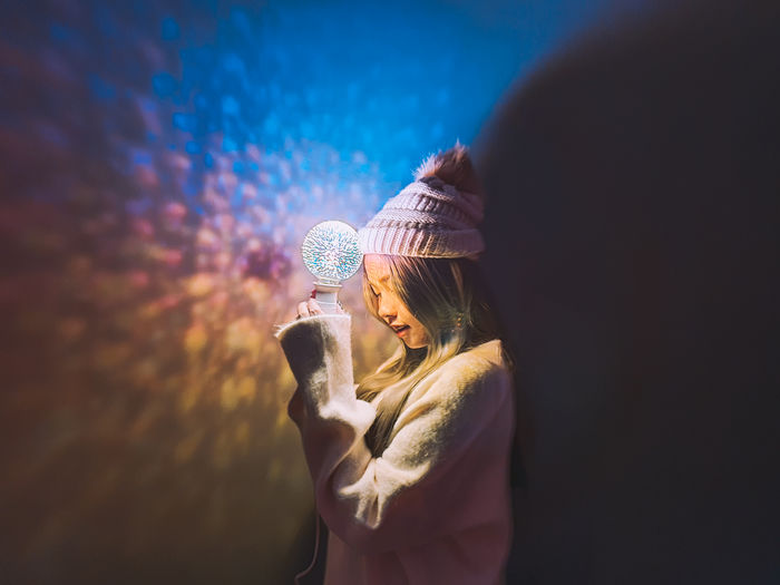 Side view of woman standing against illuminated wall