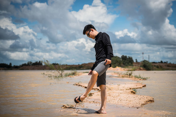 Young man standing at beach against sky