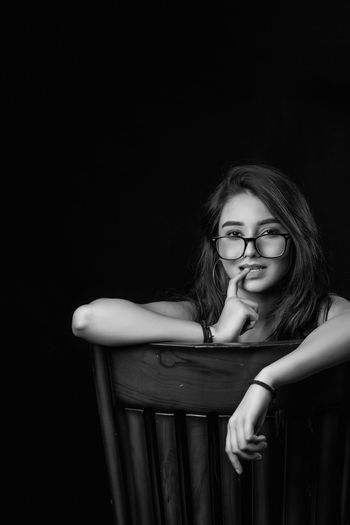 Portrait of young woman sitting on chair against black background