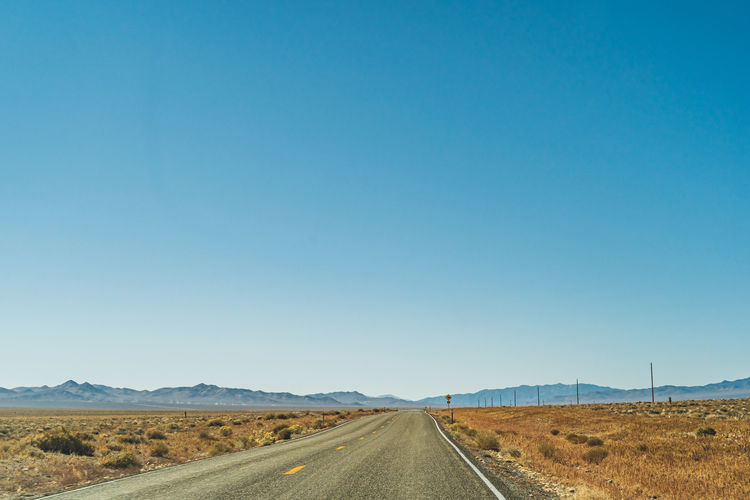 Road amidst desert against clear blue sky