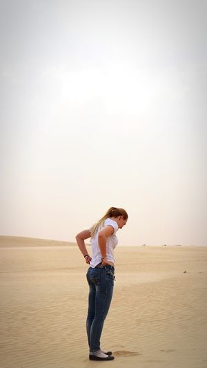 Full length of woman pulling jeans while standing on sand in desert
