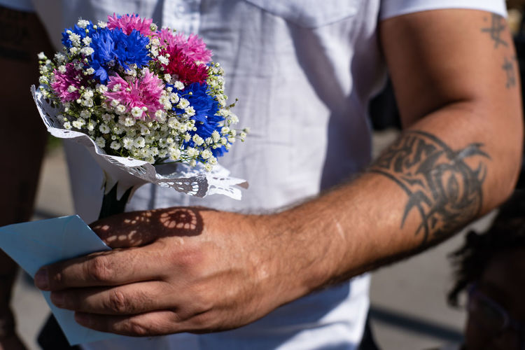 Midsection of man holding flower bouquet with tatoo.
