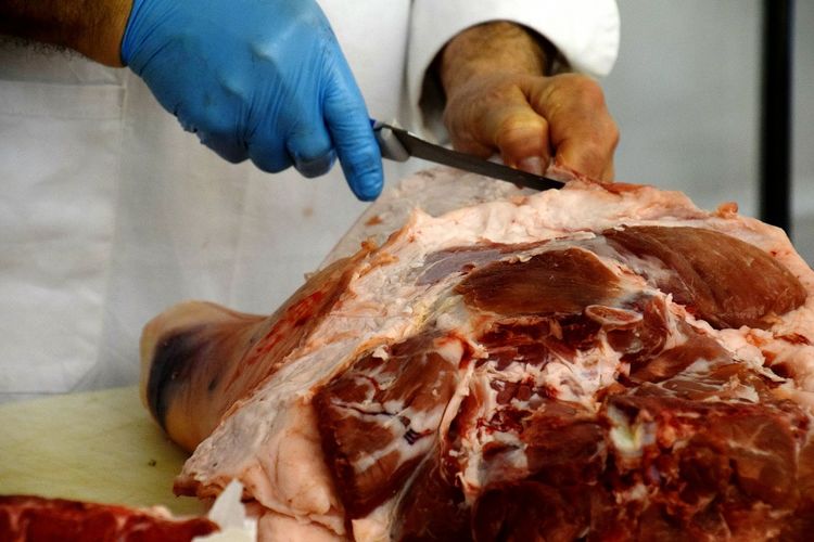 Midsection of male butcher cutting raw meat on table