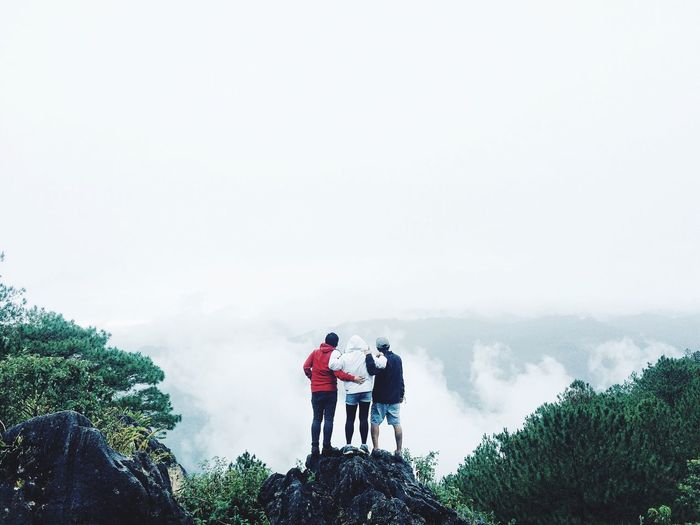 Rear view of friends standing on mountain against sky during foggy weather