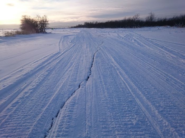Tire tracks on snow covered field against sky