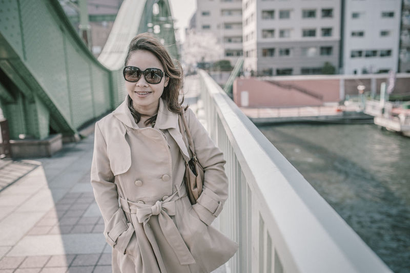 Portrait of woman in sunglasses standing against buildings in city
