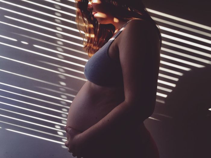 Sunlight falling on pregnant woman standing by wall