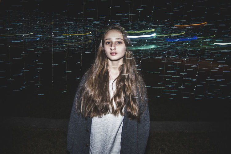 Double exposure of light trails and teenage girl on field at night