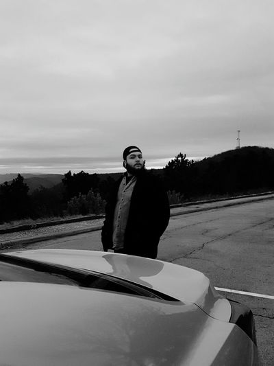 Portrait of man standing by car against cloudy sky