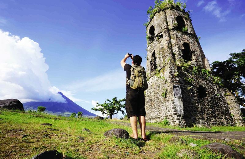 Rear view full length of man photographing mt mayon against sky on sunny day