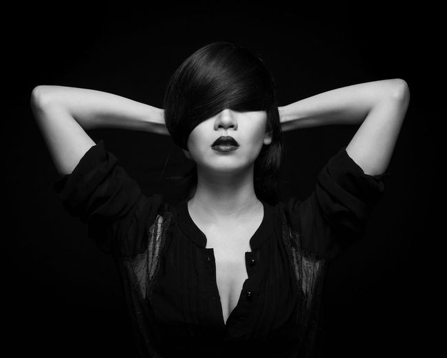 Woman with bangs standing against black background
