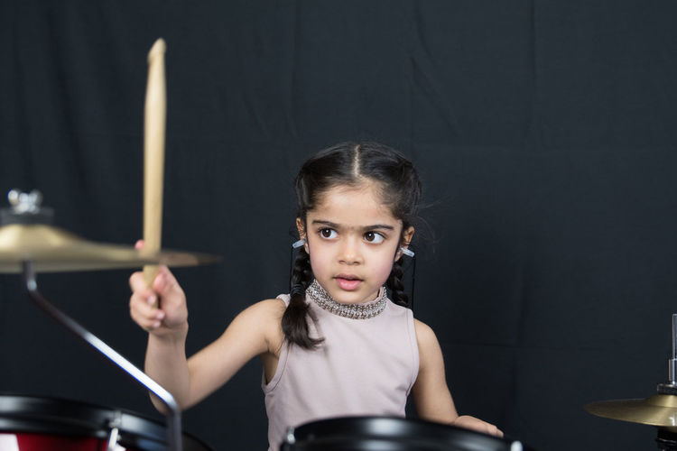Girl playing drum while standing against curtain