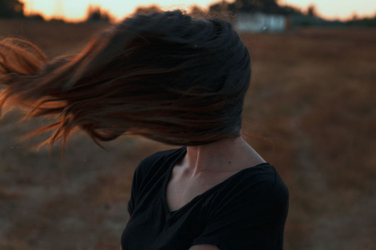 Anonymous female with hair covering face by a strong wind while standing in meadow in nature