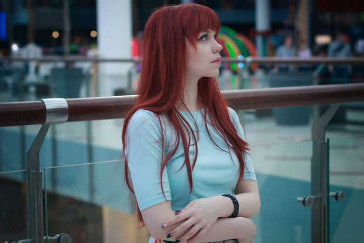 Thoughtful young woman looking away while standing by railing in shopping mall