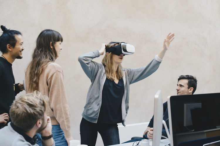 Female computer programmer using vr glasses while standing with colleagues in office