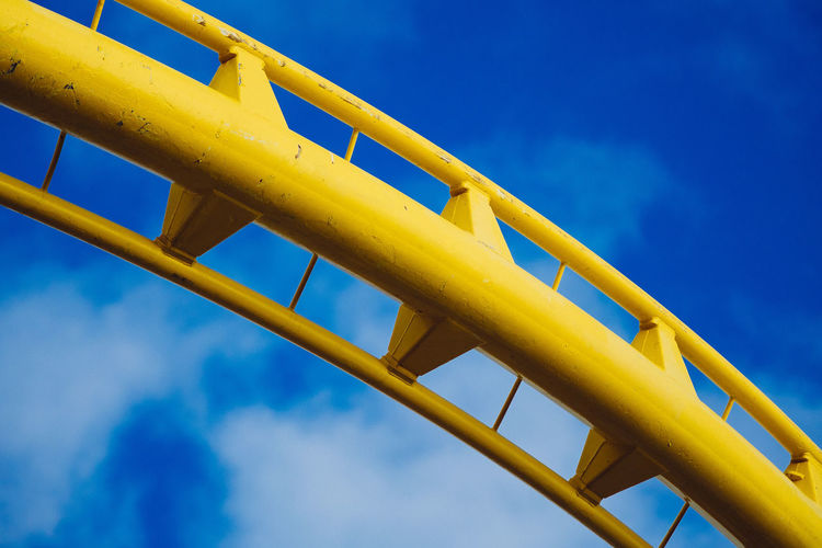 Low angle view of yellow rollercoaster against blue sky