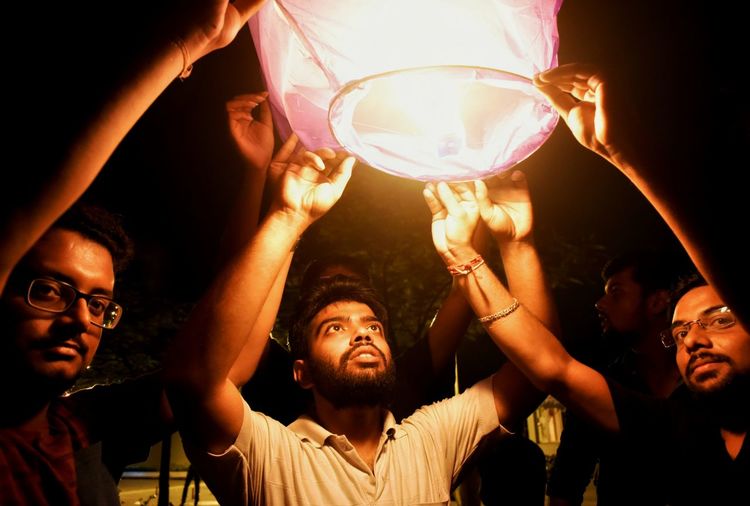 Male friends holding lit paper lantern at night