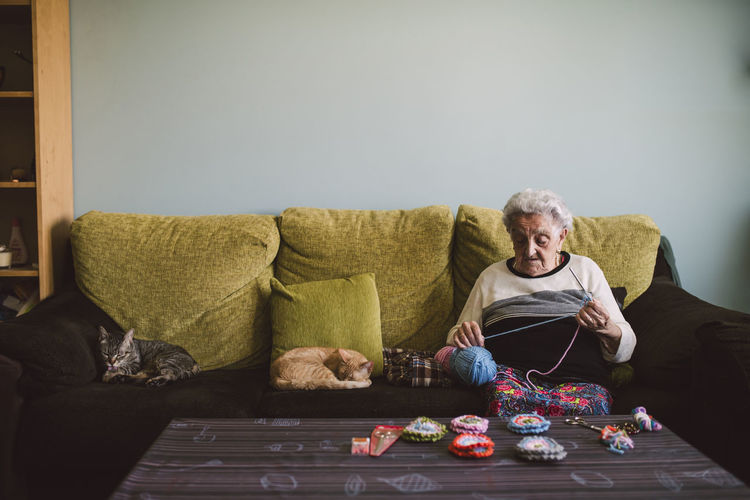 Crocheting senior woman sitting on couch besides her sleeping cats