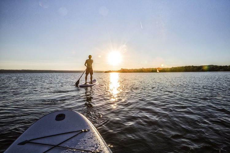 Man paddleboarding in sea against sky during sunset