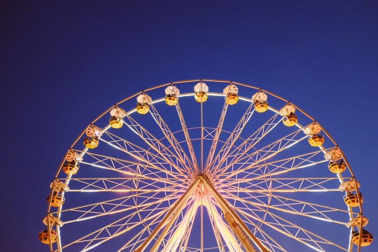Low angle view of illuminated ferris wheel against clear blue sky at night