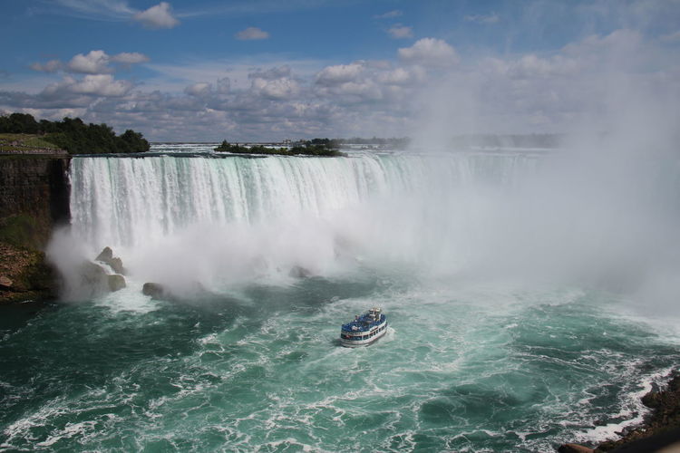 Scenic view of waterfall against sky at niagara falls . adventurous  tourists ride maid of the mist. 