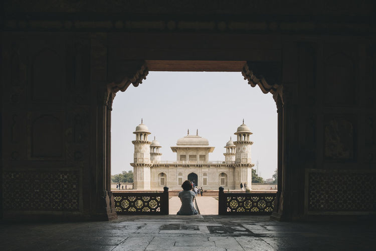 Young woman sitting at the entrance gate of the tomb of itmad-ud-daula with the mausoleum in the background.