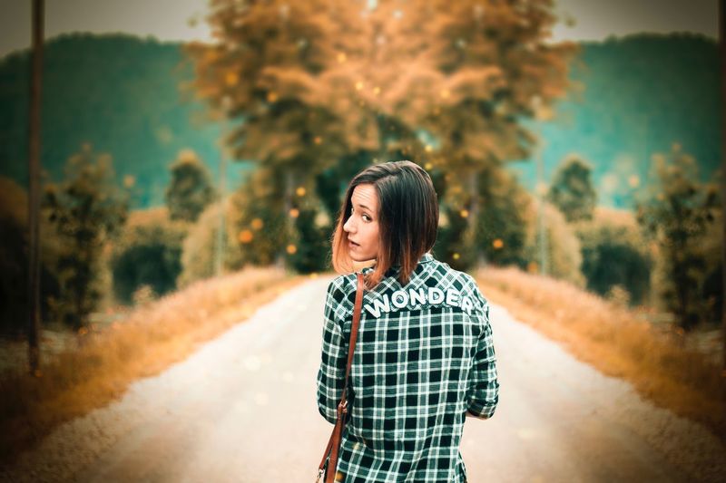 Portrait of smiling young woman standing on road against trees