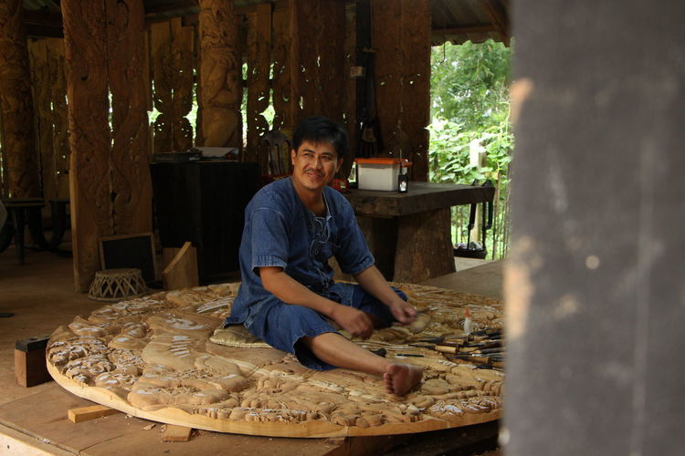 Man carving wood while sitting at workshop