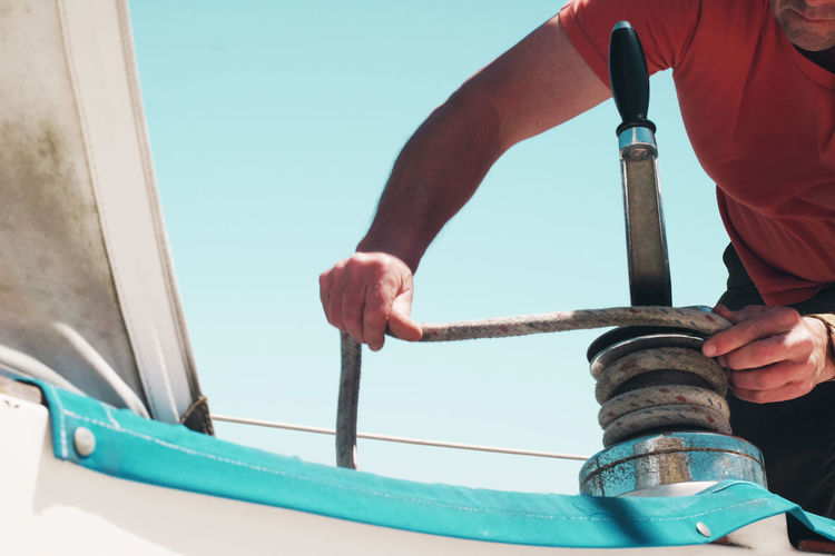 Cropped image of man tying rope on sailboat